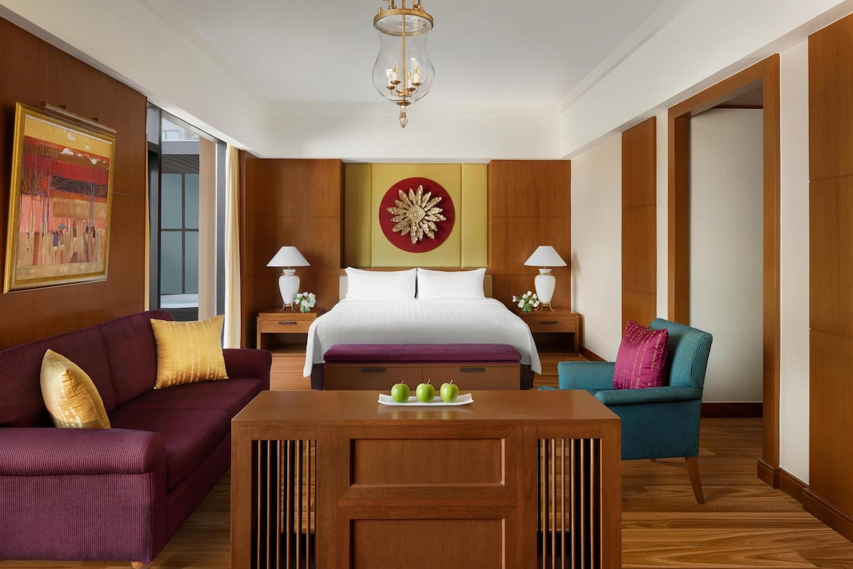 A hotel room with a large bed, a wooden desk with apples, a sofa, and a chair.