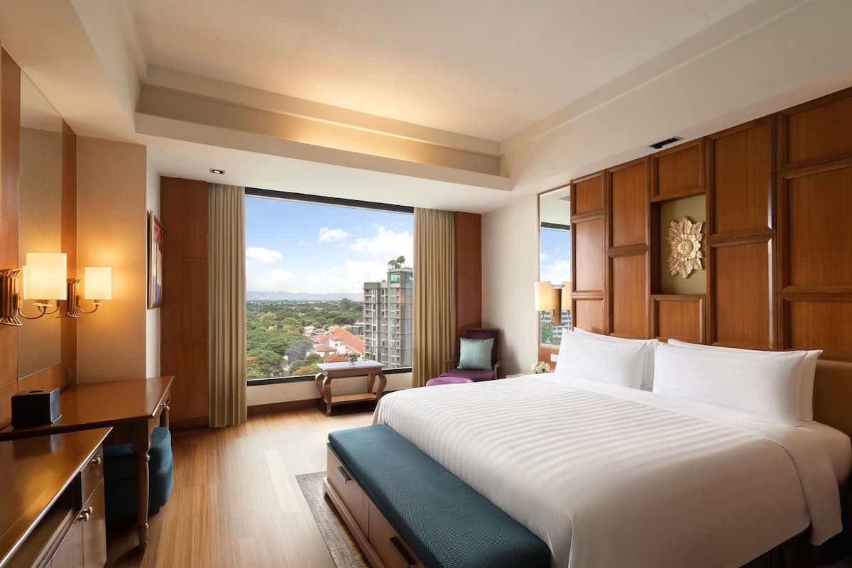 A hotel room with a large bed, a desk, a chair, and a view of a cityscape.