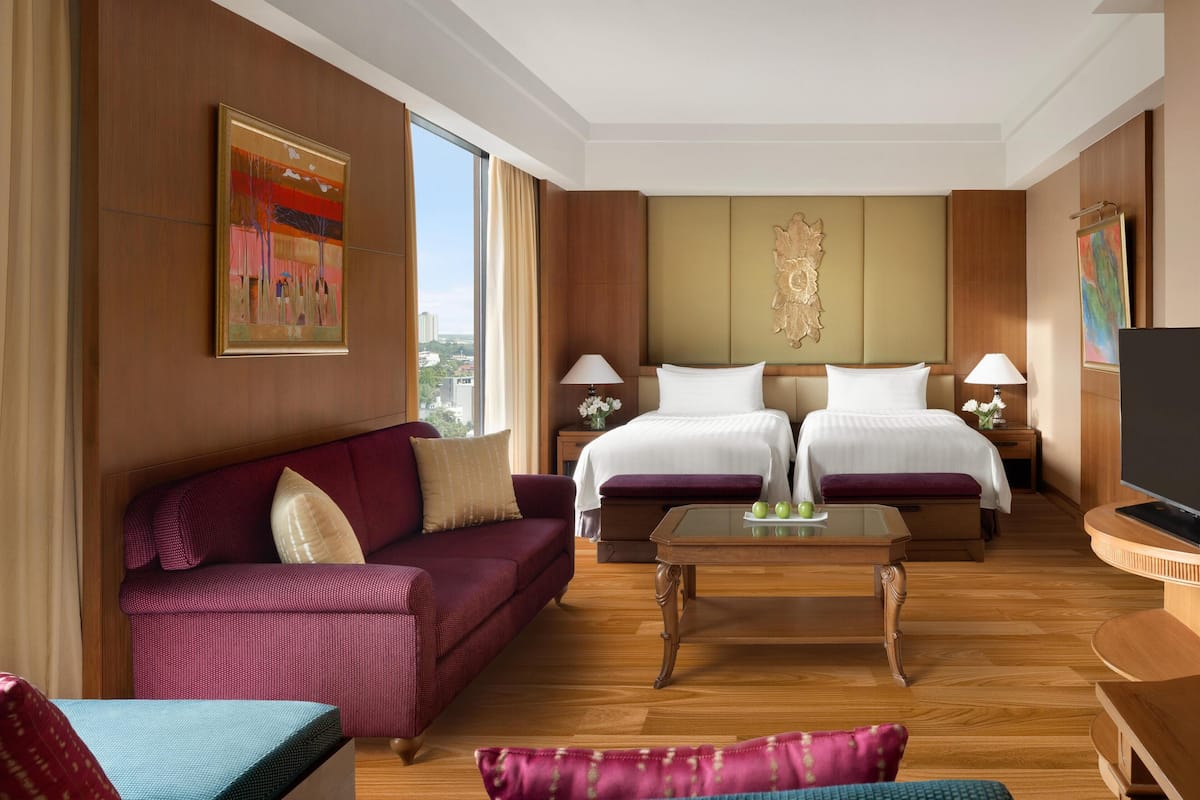 A hotel room with two beds, a sofa, a coffee table, and a TV.