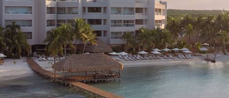 Un resort con un muelle de madera que lleva a una playa, palmeras y un edificio con techo de paja.