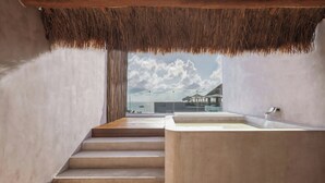 Une salle de bain moderne avec une grande baignoire, un escalier menant à un balcon et une vue sur la mer.