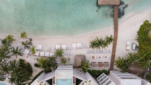 Vue aérienne d’un complexe hôtelier avec une plage, des palmiers et un espace piscine.