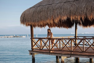 Una terraza de madera con techo de paja, con vistas a aguas tranquilas.