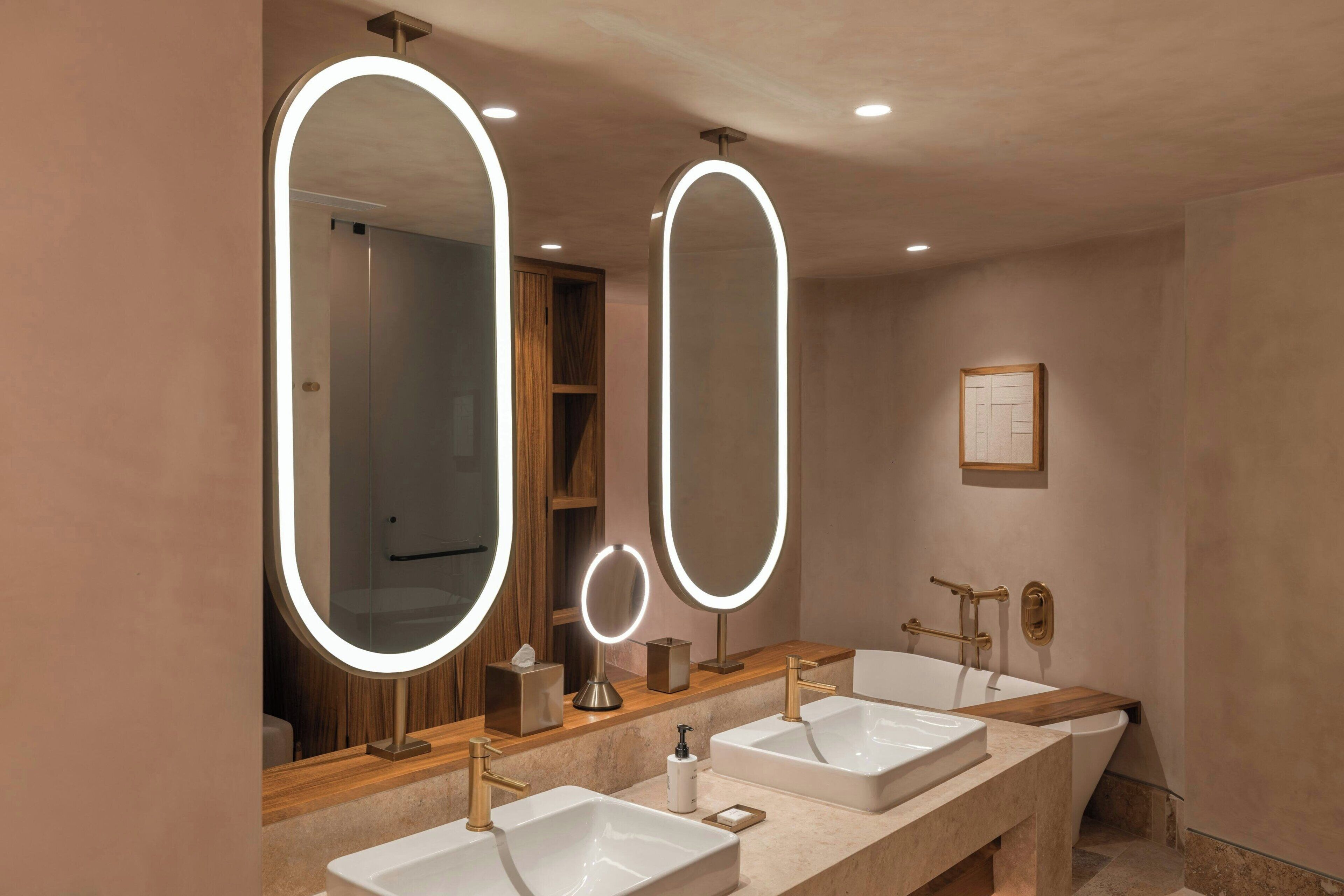 Une salle de bain moderne avec deux vasques, un grand miroir doté d’un éclairage intégré et un meuble-lavabo en bois.