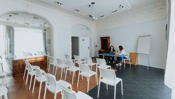 Un salón de conferencias con sillas blancas dispuestas en filas, una mesa de madera y una pizarra.