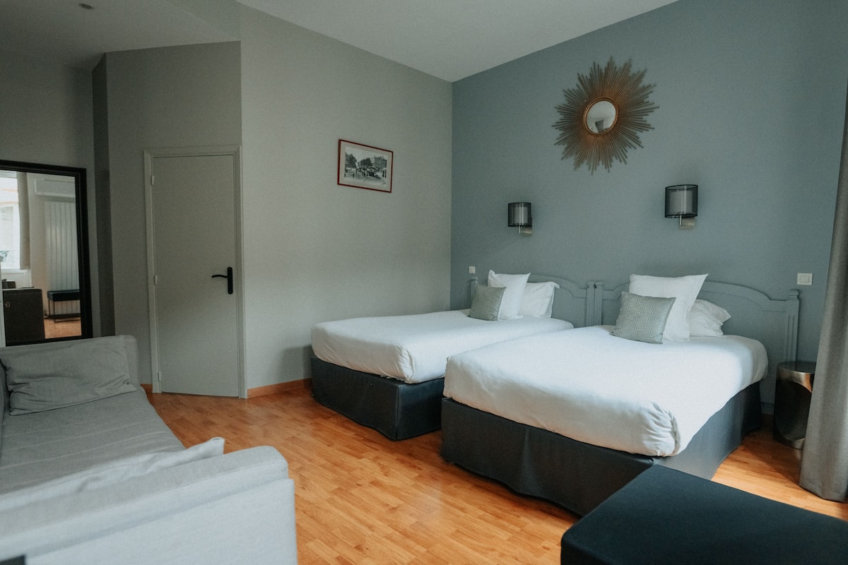 A hotel room with two single beds, a sofa, a small table, and a mirror.