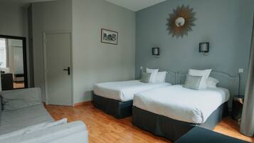 A hotel room with two single beds, a sofa, a small table, and a mirror.