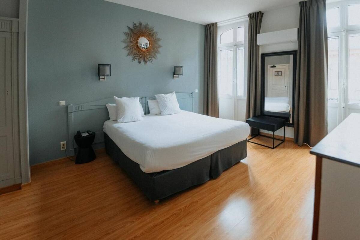 A bedroom with a large bed, two bedside lamps, a mirror, and a view of the outside.