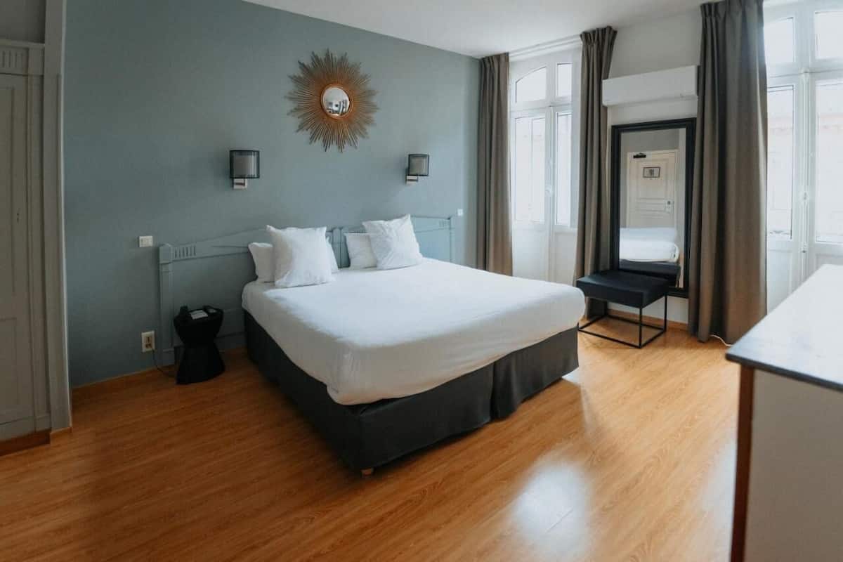 A bedroom with a large bed, two bedside lamps, a mirror, and a view of the outside.
