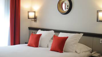 A hotel room with a large bed, red and white pillows, a bedside table with a phone, and a wall-mounted mirror.