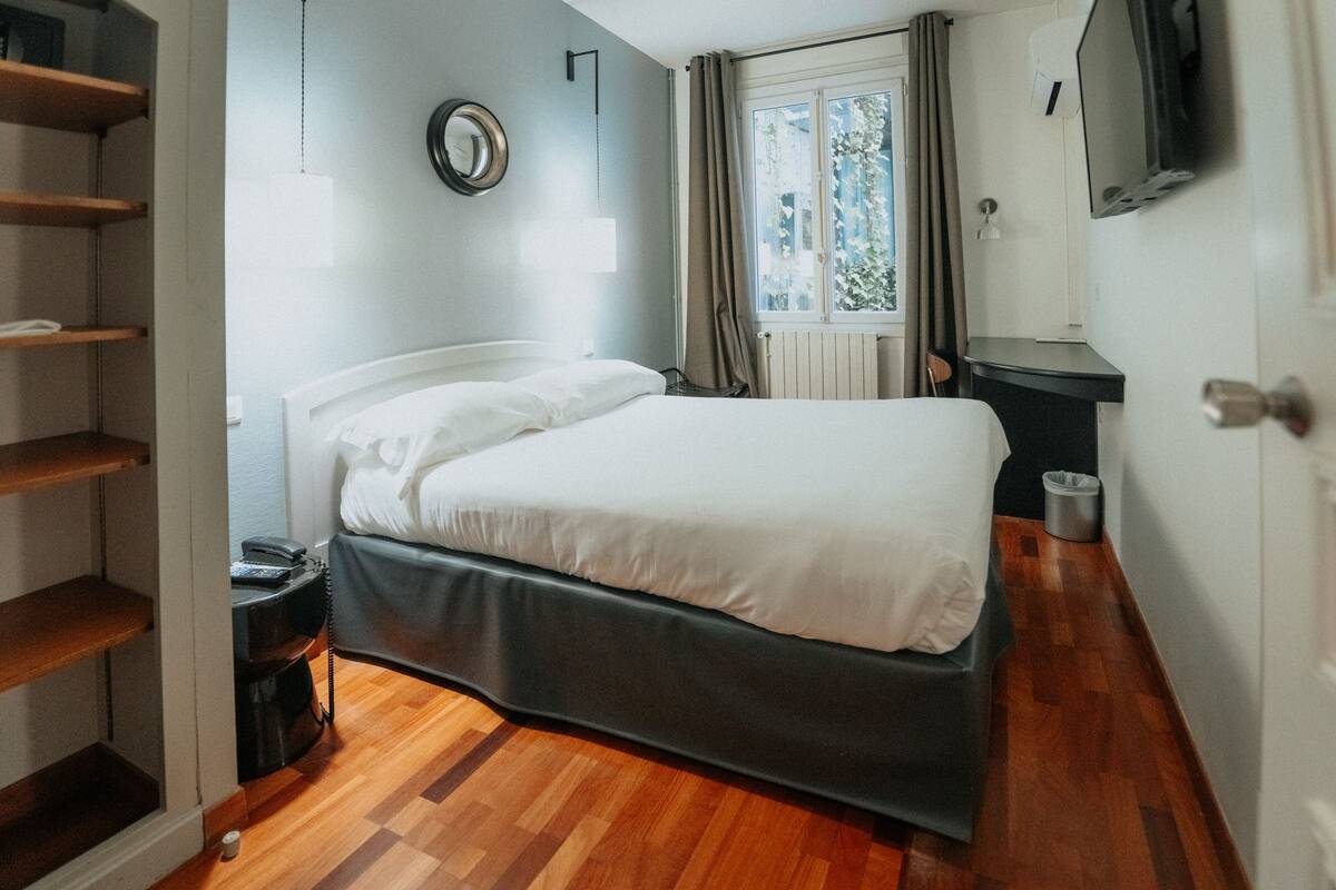 A bedroom with a bed, a wardrobe, a TV, and a window with curtains.