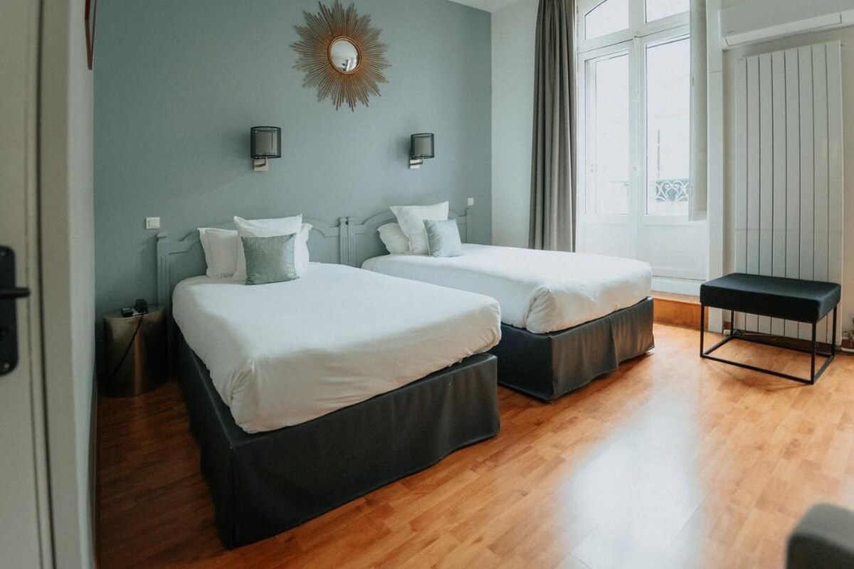 A double room with two beds, a bench, and a large window.