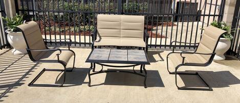 A patio area with a metal table and two beige cushioned chairs.