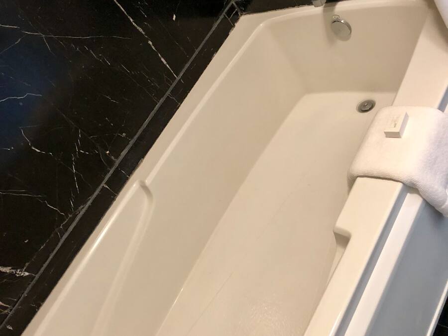 Une baignoire à l’intérieur blanc, avec un robinet chromé et une serviette blanche suspendue sur le bord.