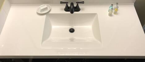 A white bathroom sink with a black faucet, a soap dish, and two bottles of hand soap.