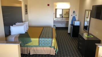 A hotel room with a bed, a desk, a mirror, and a television.