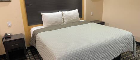 Habitación de hotel con una cama grande, una mesita de noche, un reloj de pared y un adorno decorativo en la pared.