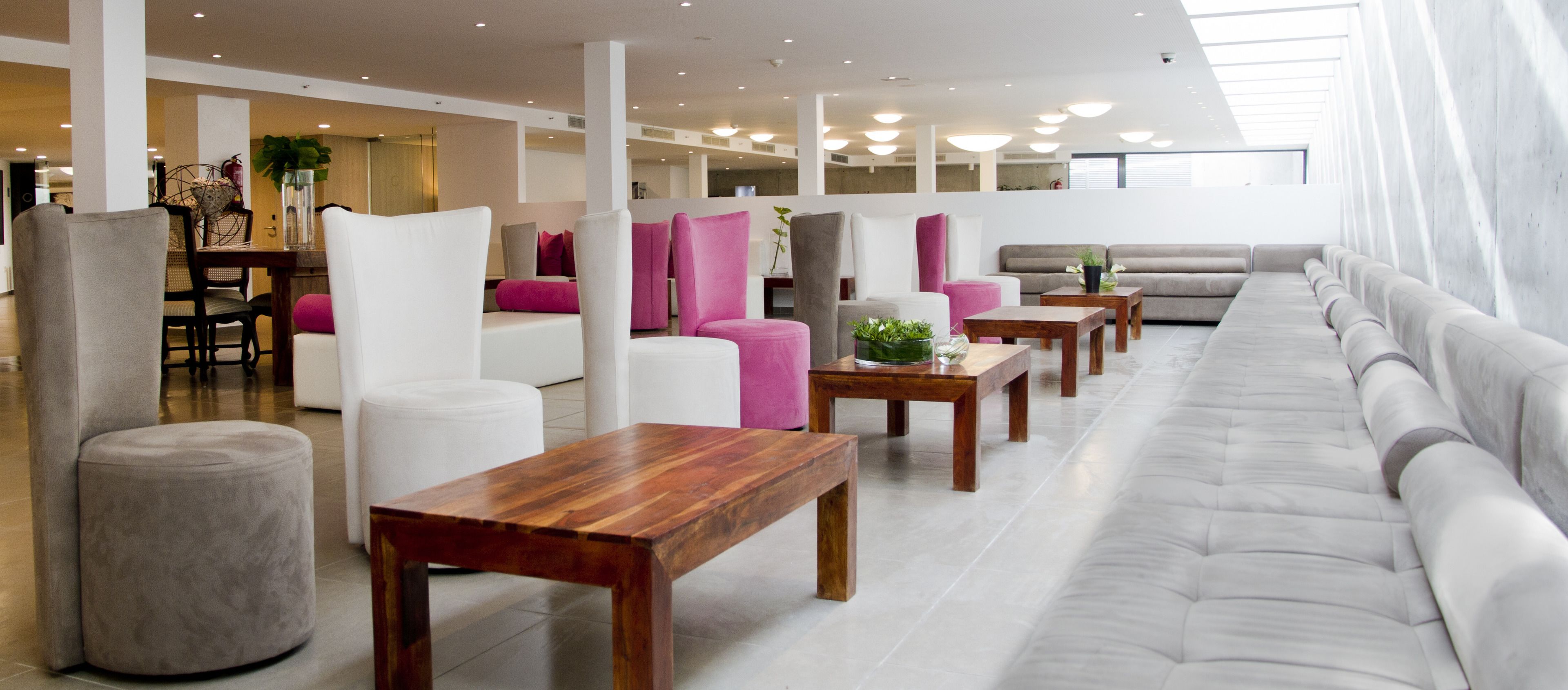 Un moderno vestíbulo de hotel con un sofá largo de color gris, sillas blancas y mesas de madera.
