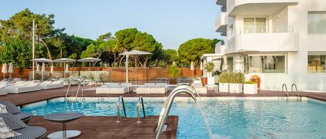 A pool area with lounge chairs, umbrellas, and a wooden deck.