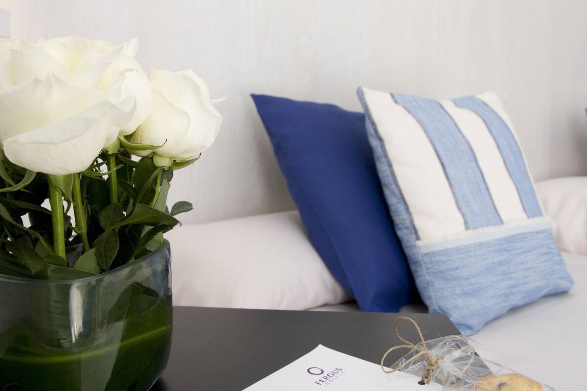 Une pièce avec un canapé blanc, un coussin à rayures bleues et blanches, un vase contenant des roses blanches et un menu posé sur une table.
