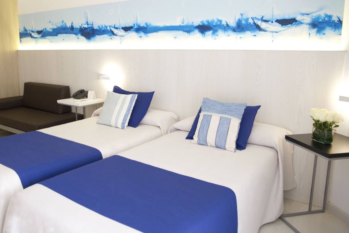 Une chambre d’hôtel avec deux lits, un canapé, une petite table avec un téléphone et un tableau au mur.