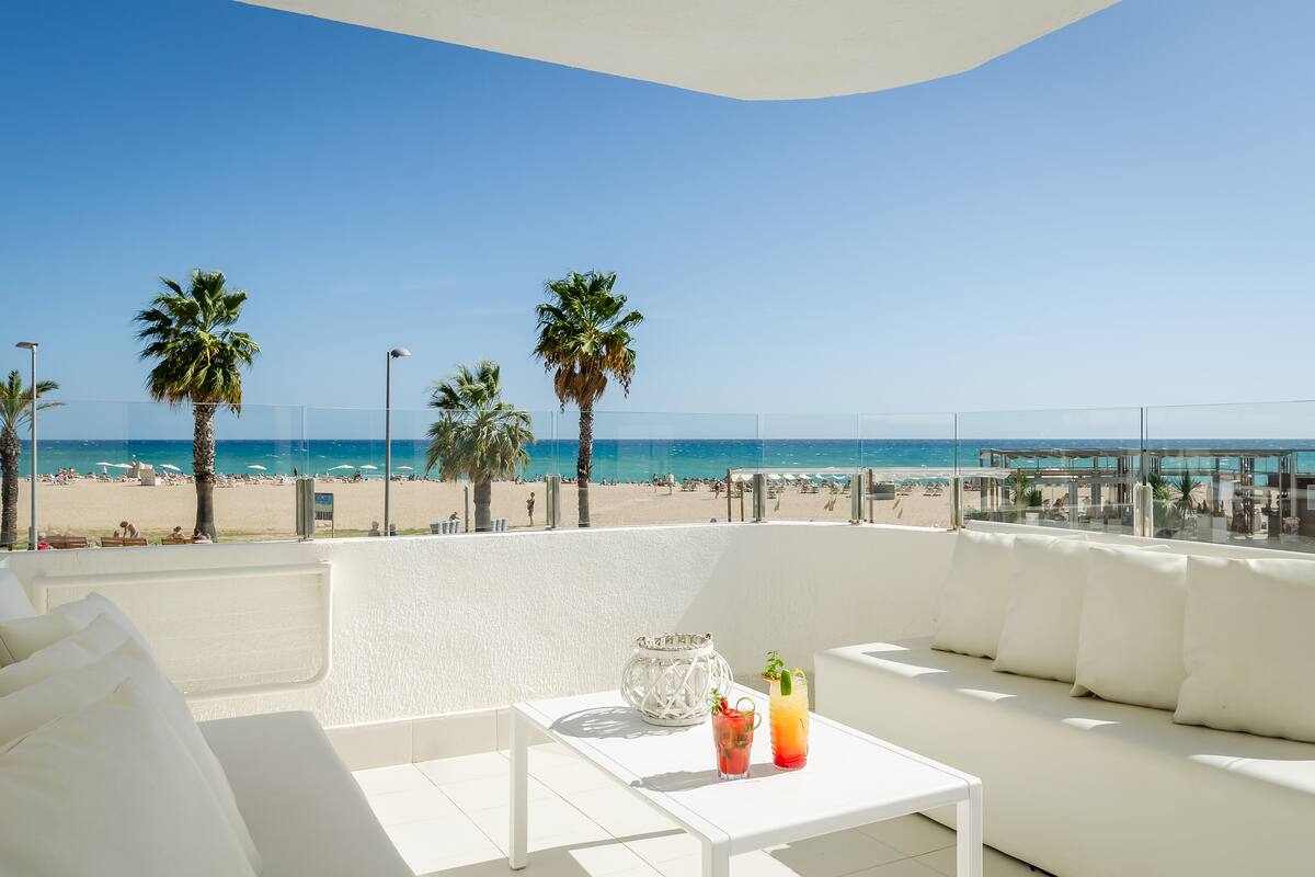 Un balcon avec un canapé blanc, une petite table et une vue sur la plage et l’océan.