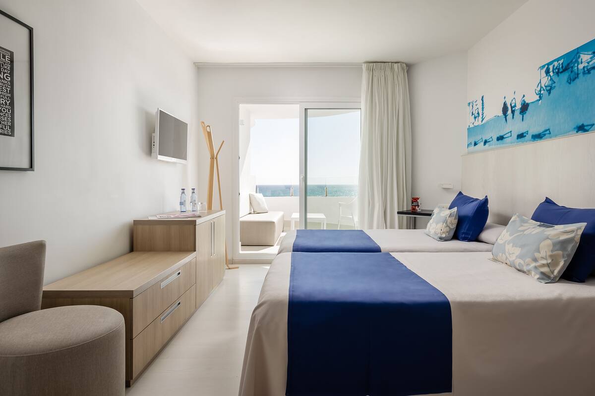 Une chambre d’hôtel avec deux lits, un bureau, une chaise, une télévision et un balcon avec vue.