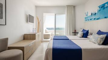 Habitación de hotel con dos camas, un escritorio, una silla, un televisor y un balcón con vistas.