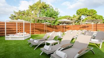 Un patio trasero con mobiliario exterior, incluyendo sillones de descanso y sombrillas, y una valla de madera.