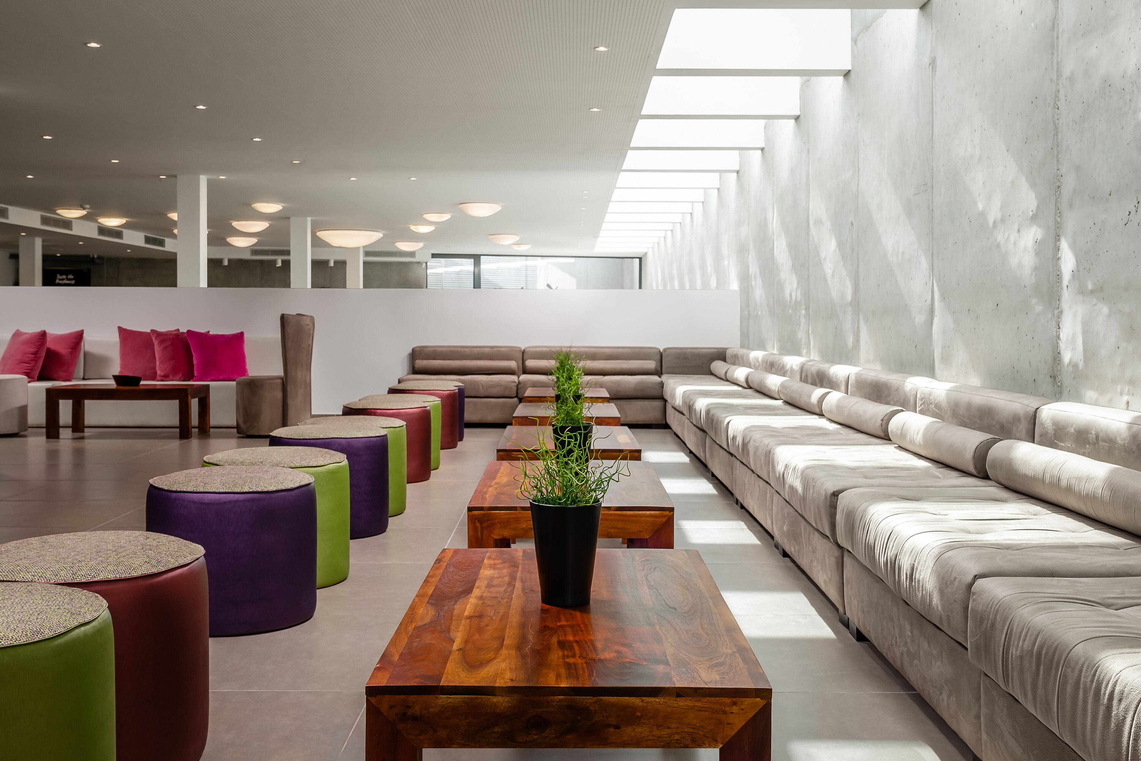 Un espace de détente moderne avec un long canapé, des poufs colorés et des tables en bois.