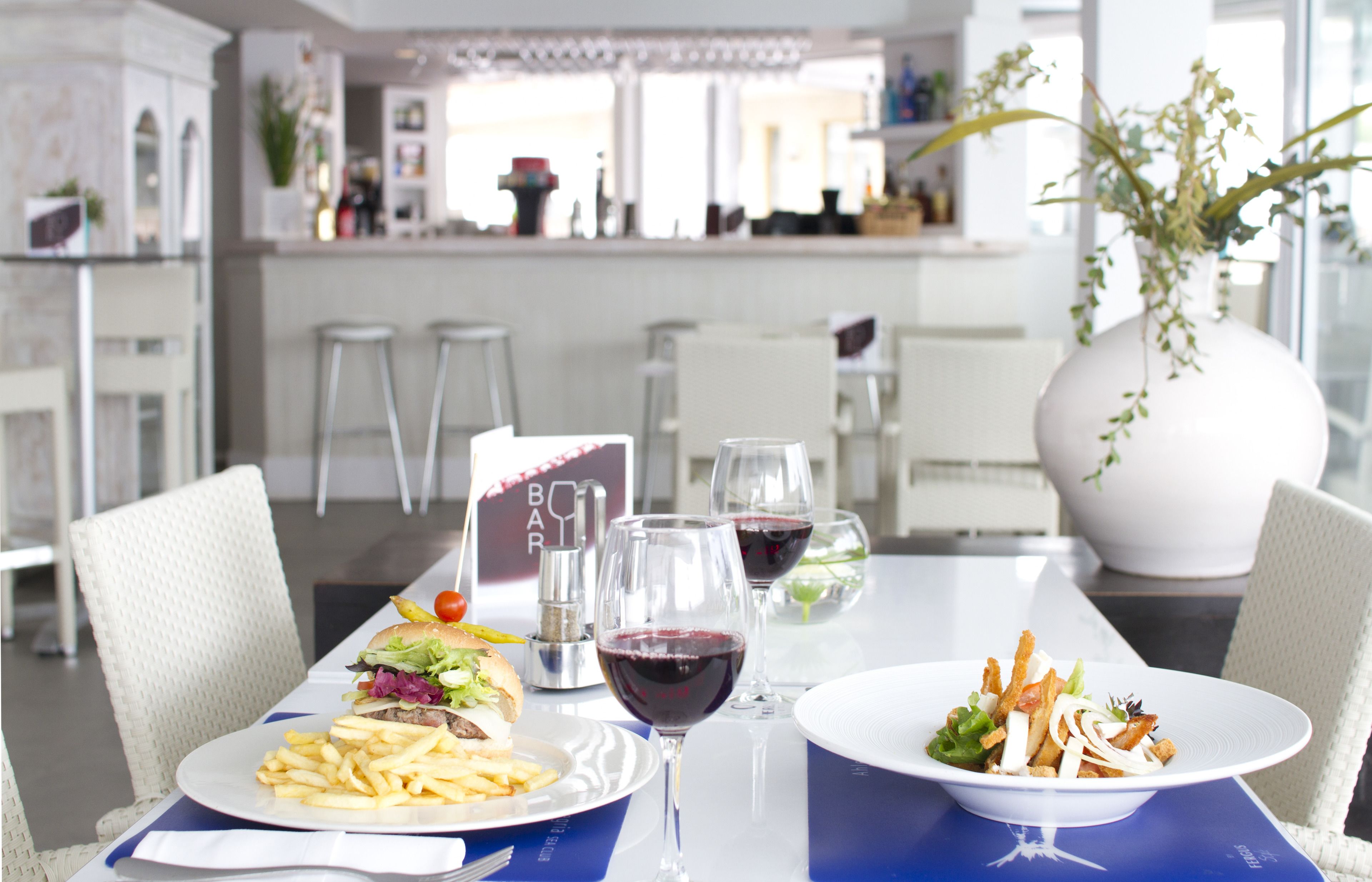A dining table with a burger, fries, and salad, wine glasses, and a menu.