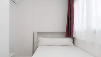 Een enkel bed met witte beddengoed, een hoofdbord en een raam met dunne gordijnen.