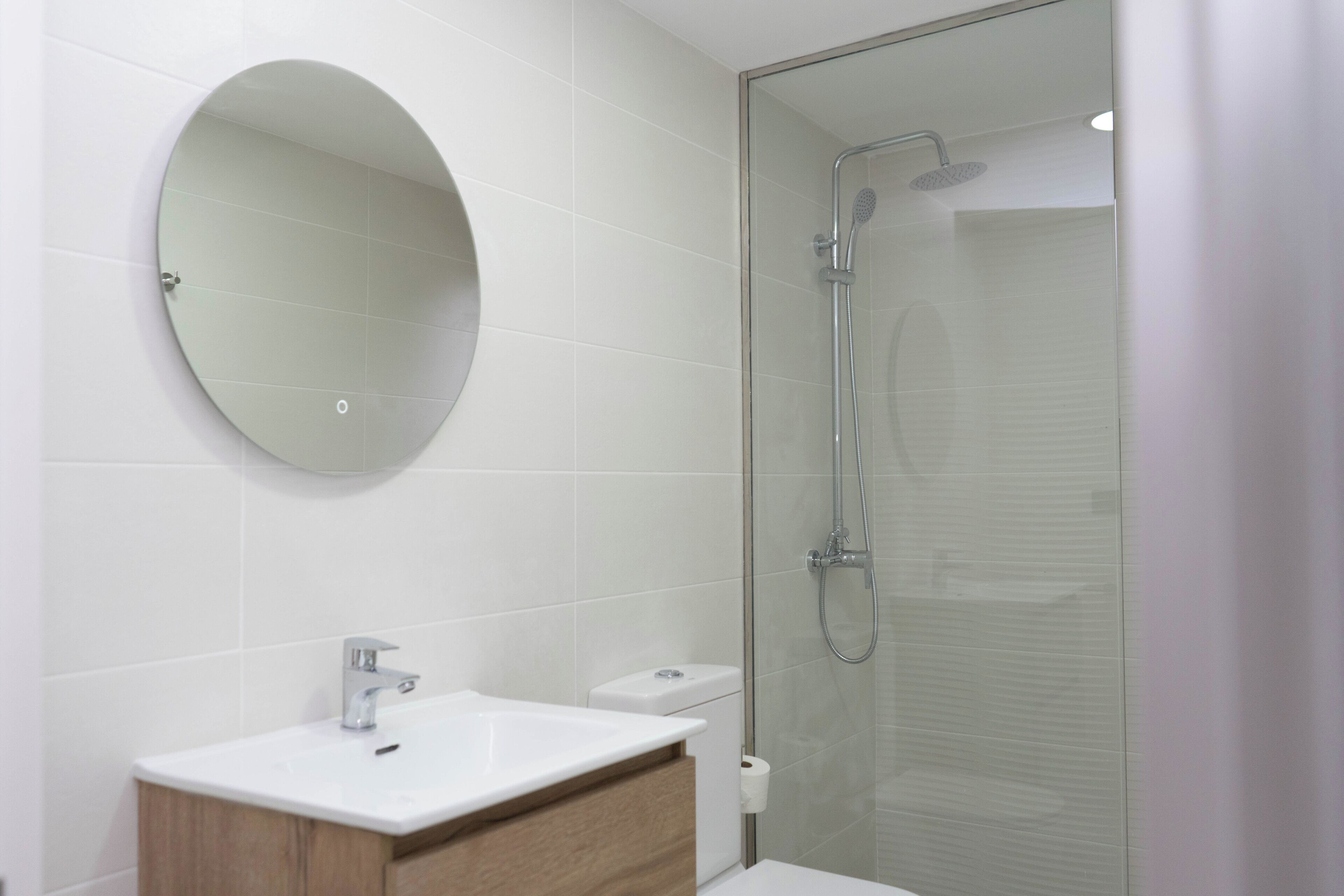 A modern bathroom with a round mirror, a sink, and a glass-enclosed shower.