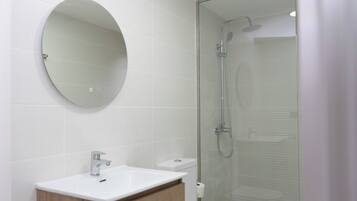 A modern bathroom with a round mirror, a sink, and a glass-enclosed shower.
