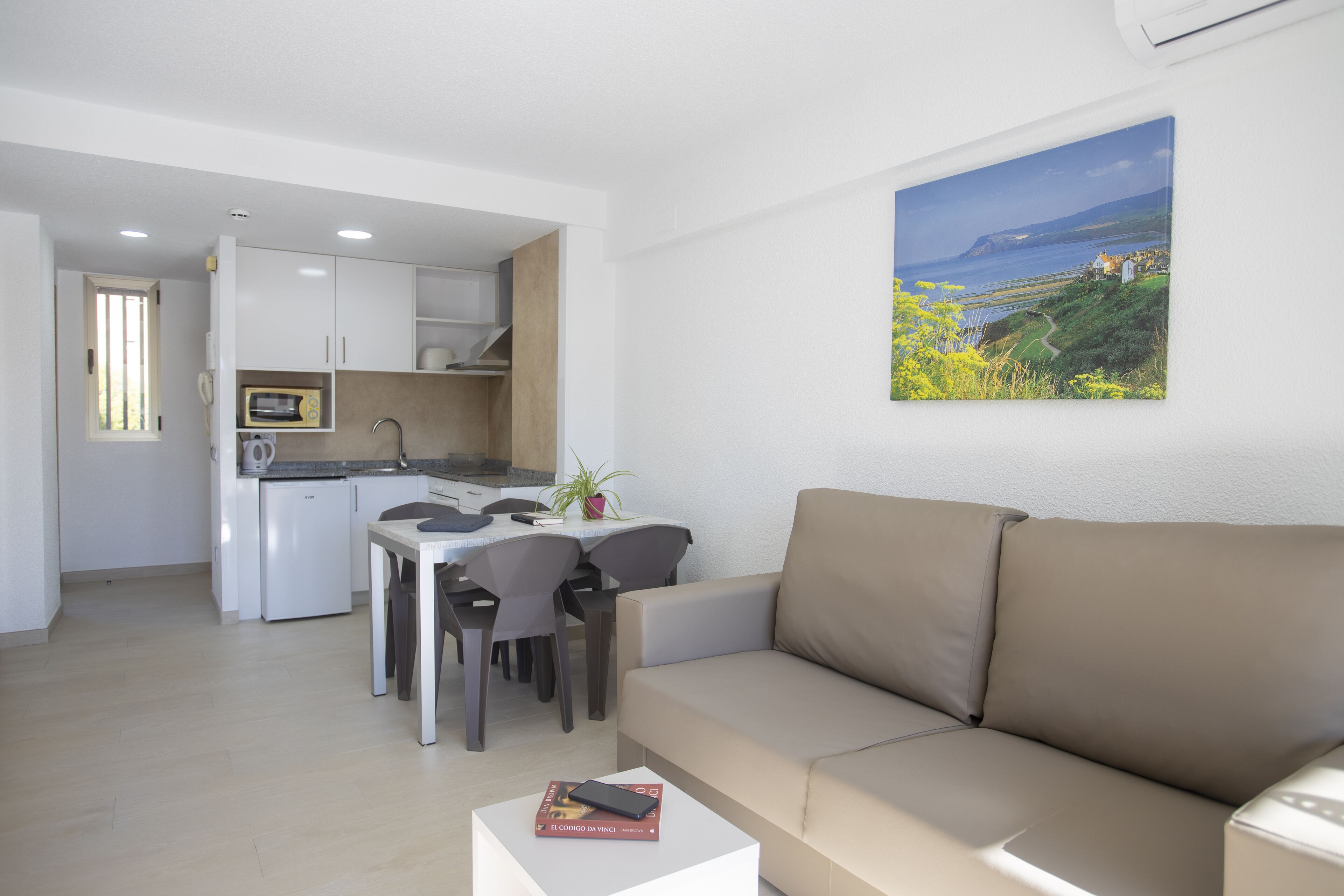 A modern apartment with a dining area, kitchenette, and a large window with a coastal view.