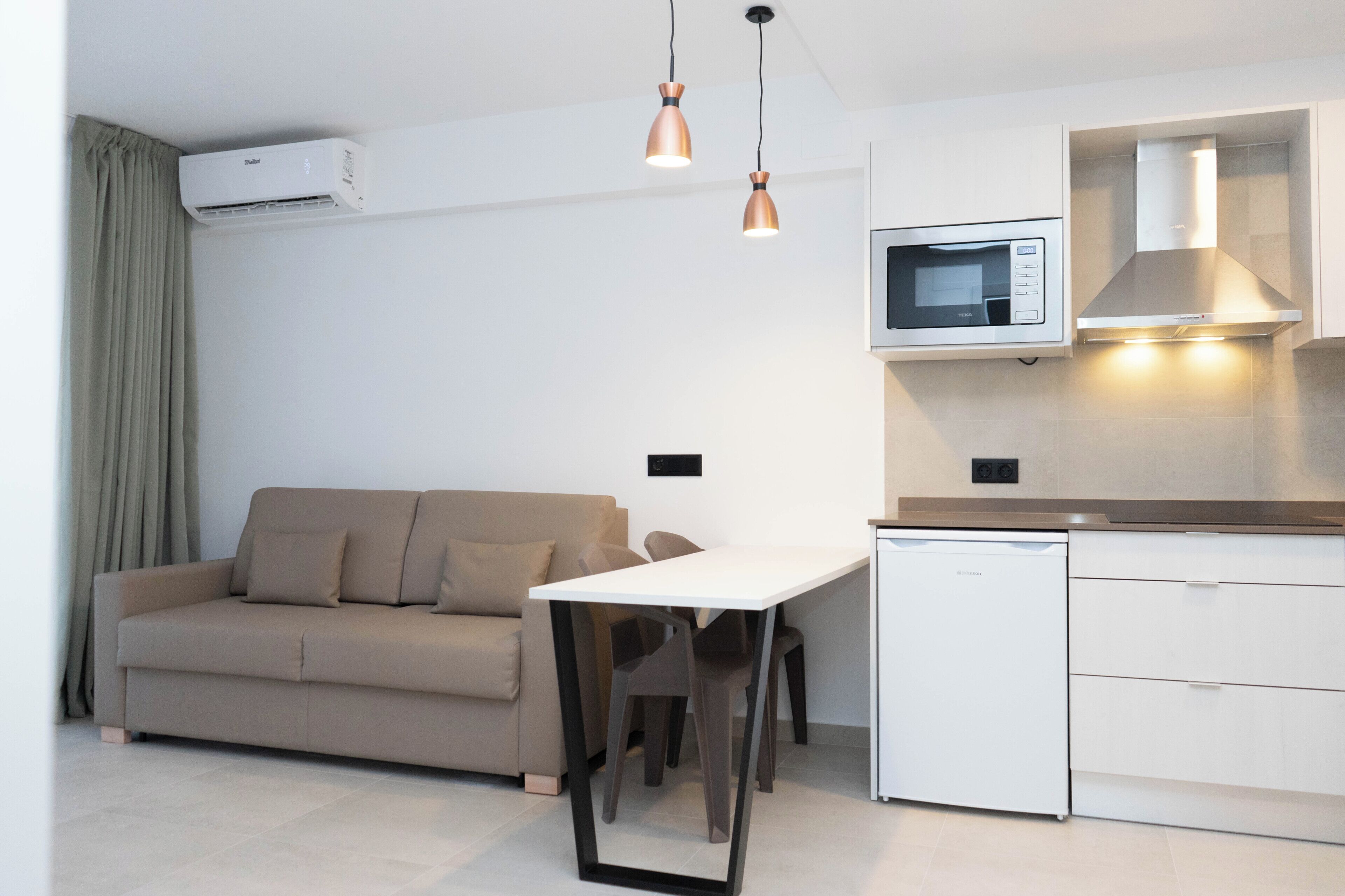 A modern kitchen with a microwave, oven, and dishwasher. There is a dining table with chairs and a sofa in the living area.