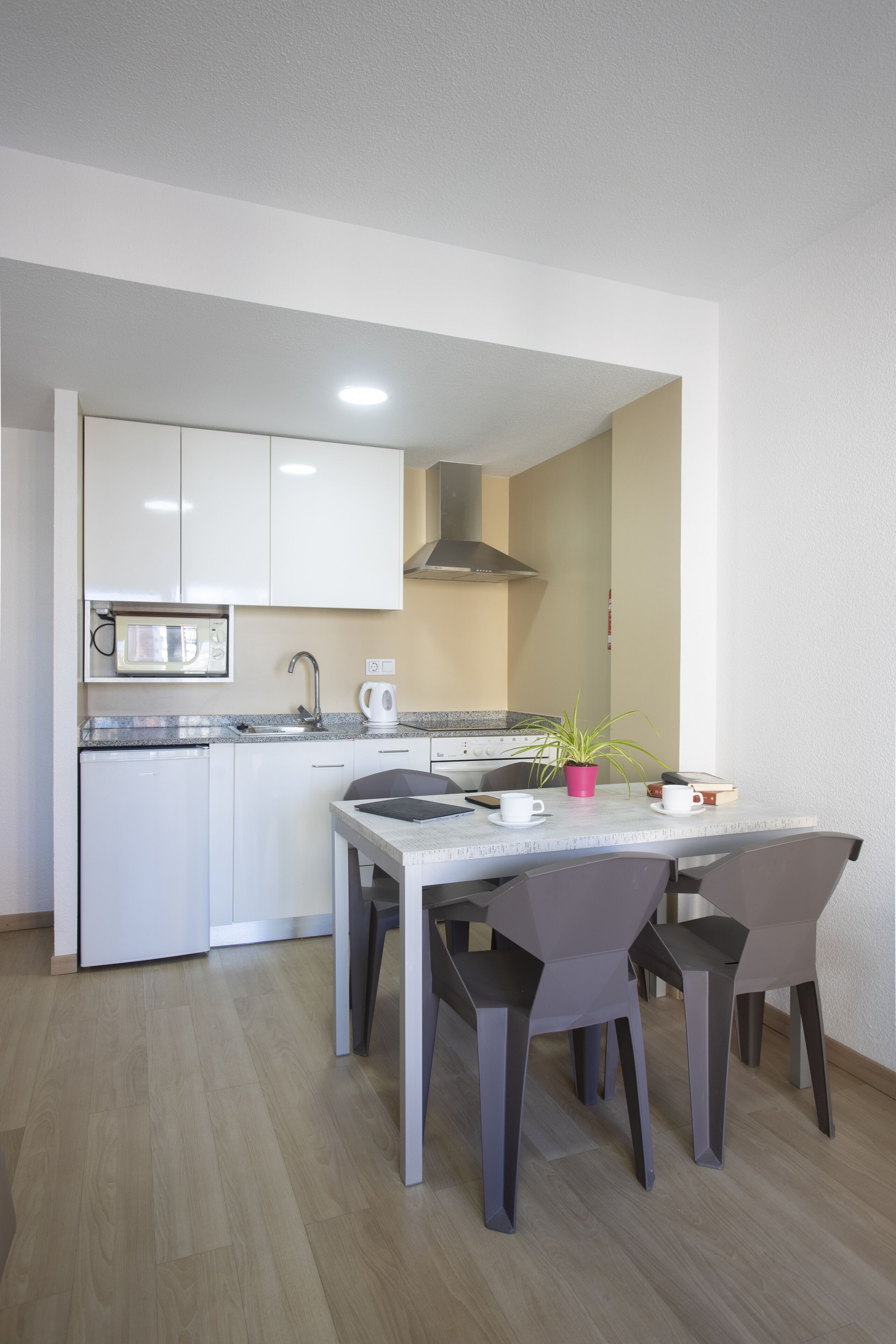 A modern kitchen with white cabinets, a microwave, a stove, and a sink. There is a dining table with four chairs and a potted plant on the table.