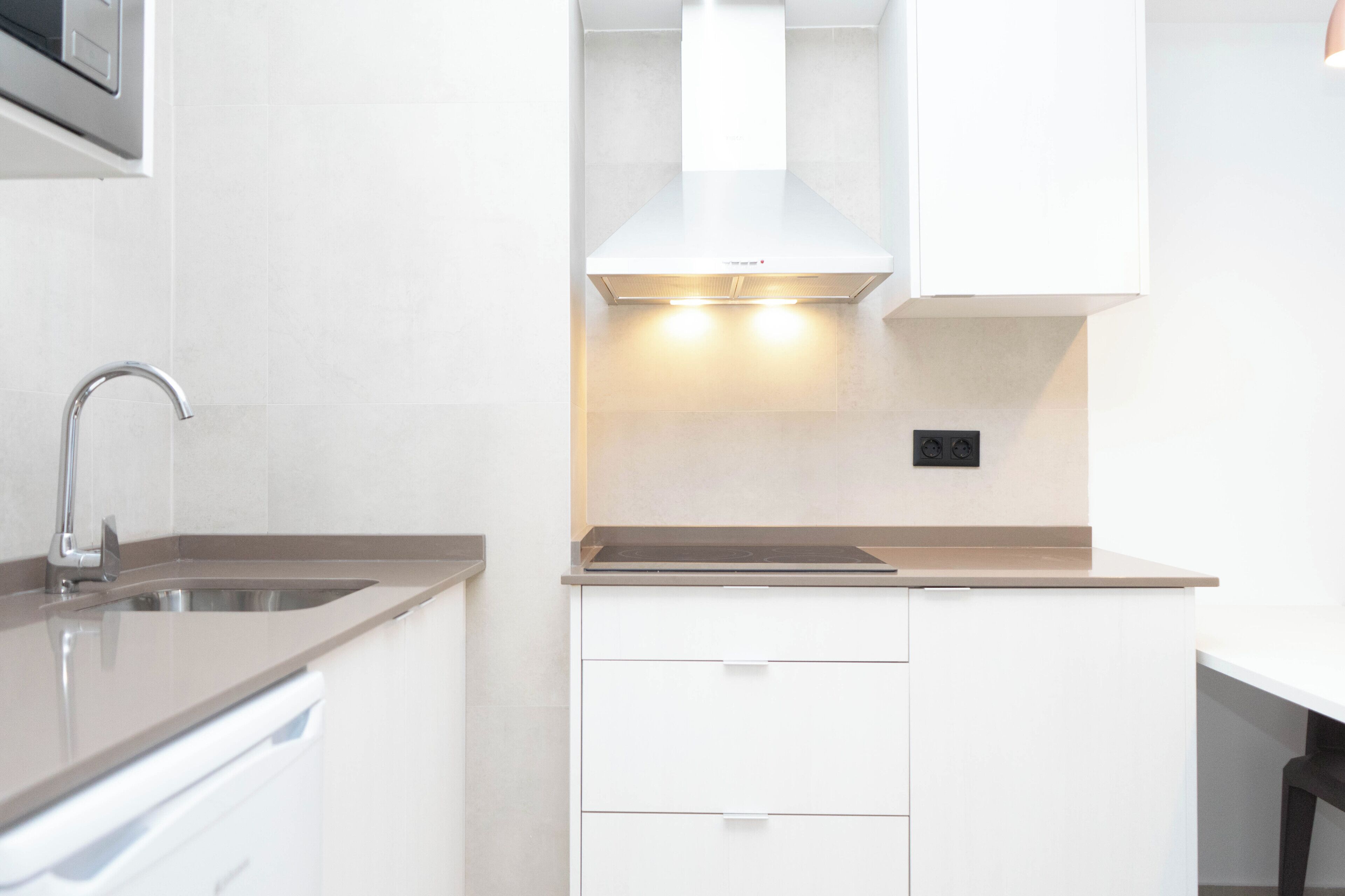 A modern kitchen with a stainless steel sink, white cabinetry, and a range hood.
