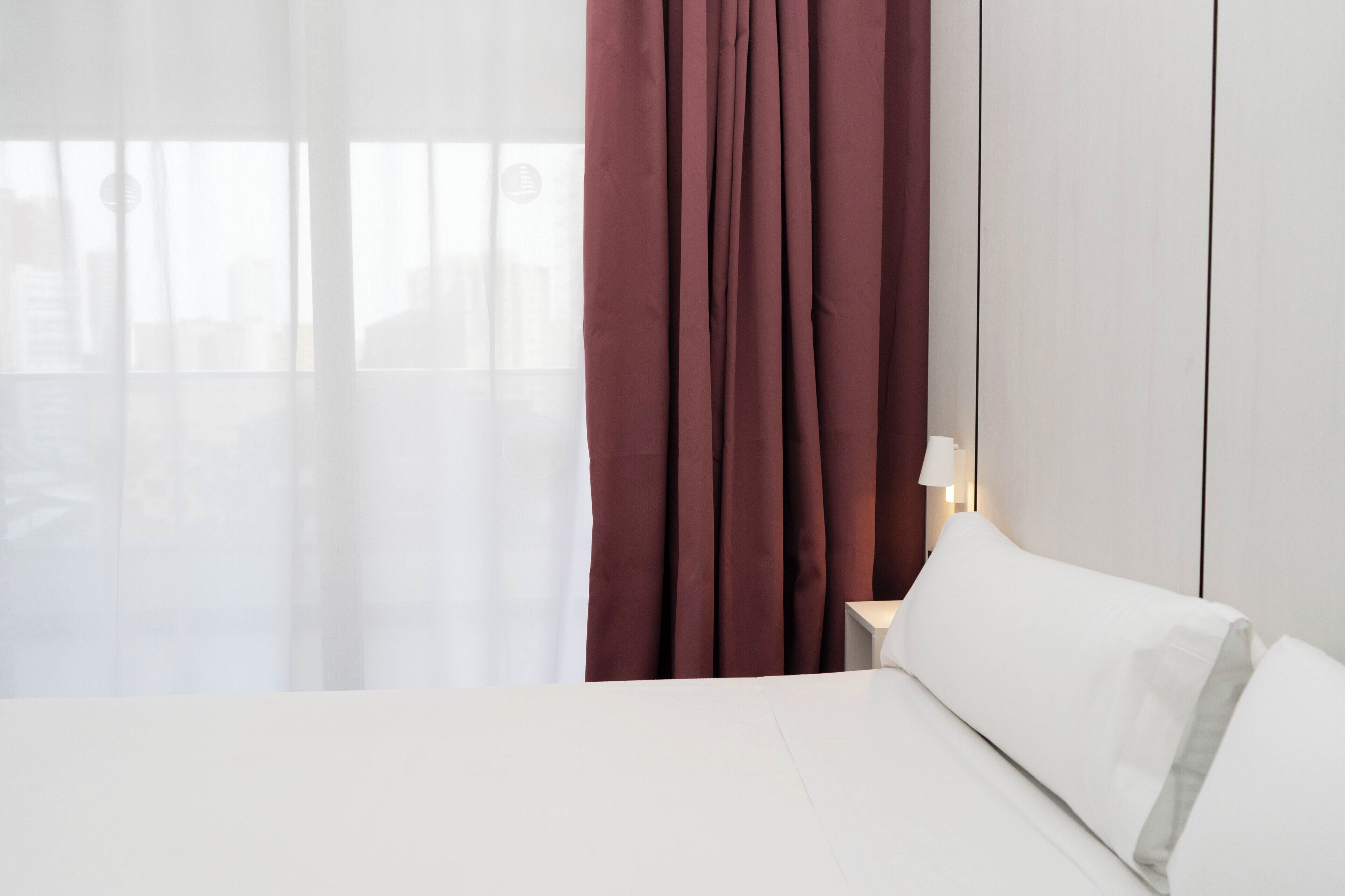 Una habitación de hotel con una cama, cortinas, una mesita de noche y una lámpara.