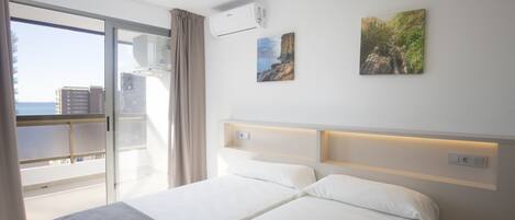 A hotel room with two beds, a balcony with a view of the city, and an air conditioning unit on the wall.