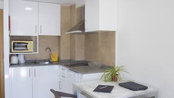 A compact kitchen with white cabinets, a microwave, a sink, and a small plant. There is a table with two chairs and a few items on it.