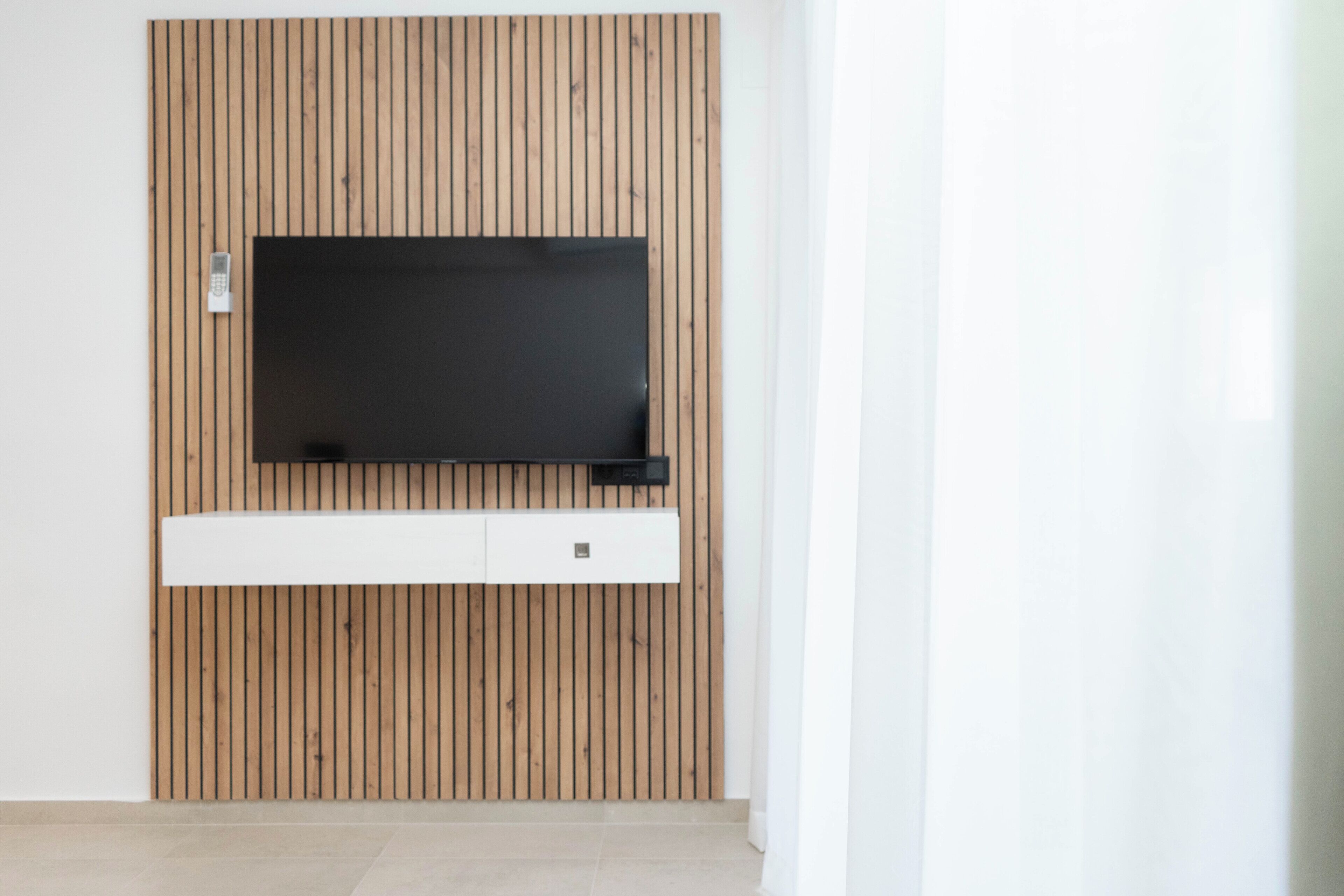 A modern room with a wooden panel wall, a mounted flat-screen TV, and a white cabinet below it.