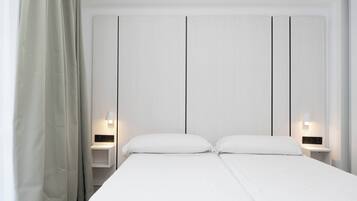 A double bed with white bedding, two bedside tables with lamps, and a plain wall with vertical lines.