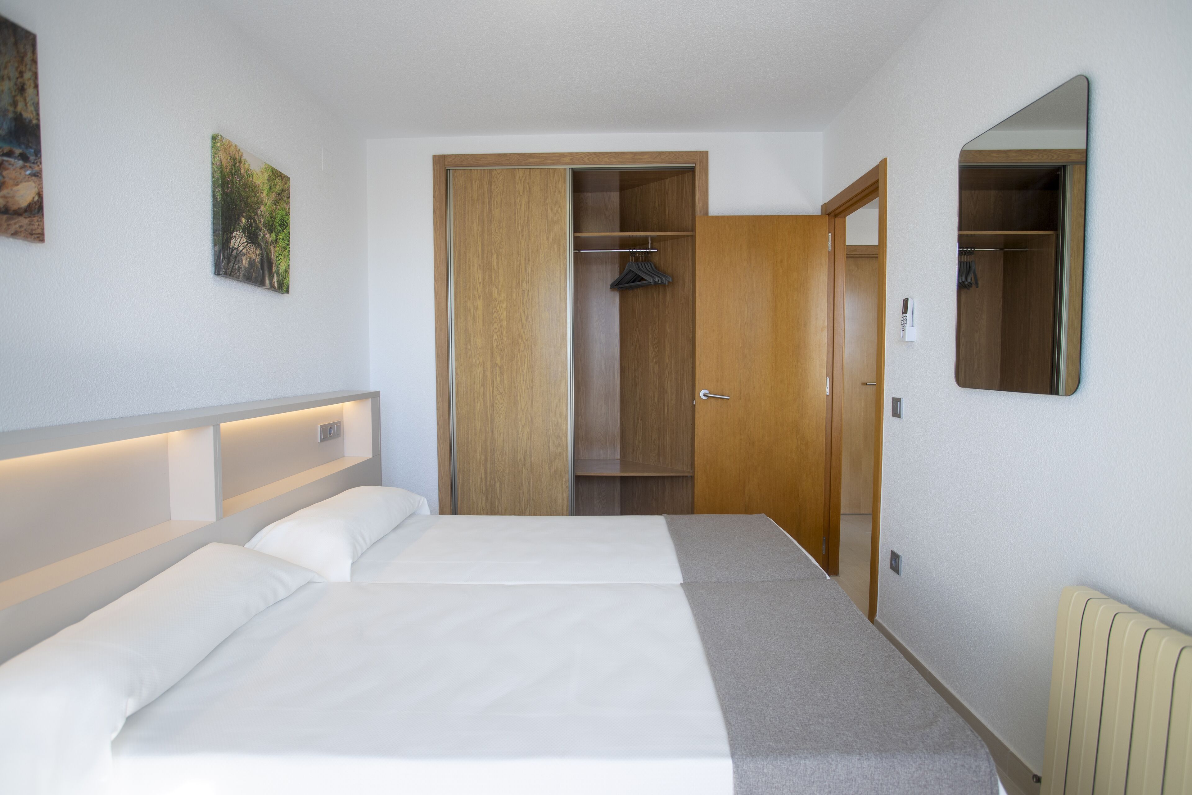A hotel room with a bed, a wardrobe, a mirror, and a radiator.