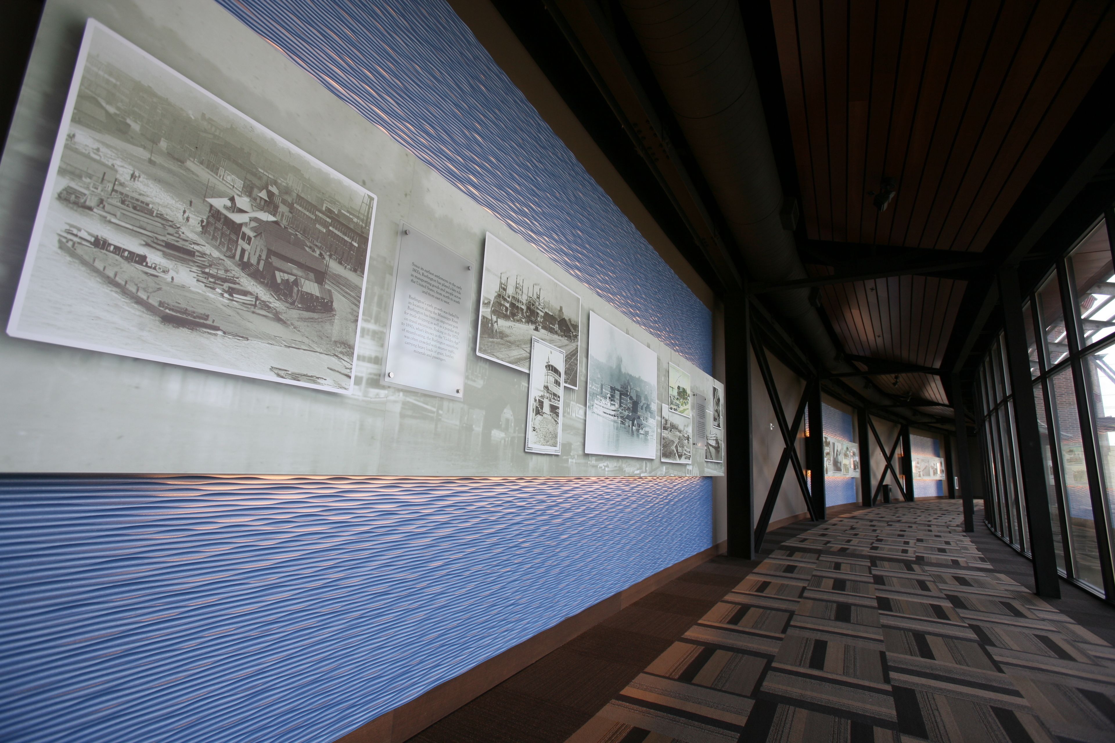 A corridor with a patterned floor, a wall with historical photographs, and a wooden ceiling.