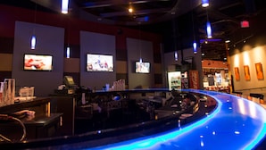 A modern bar area with a curved counter, overhead lighting, and multiple screens displaying content.