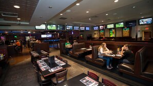 A restaurant with multiple screens displaying sports events, booths, and tables with menus.