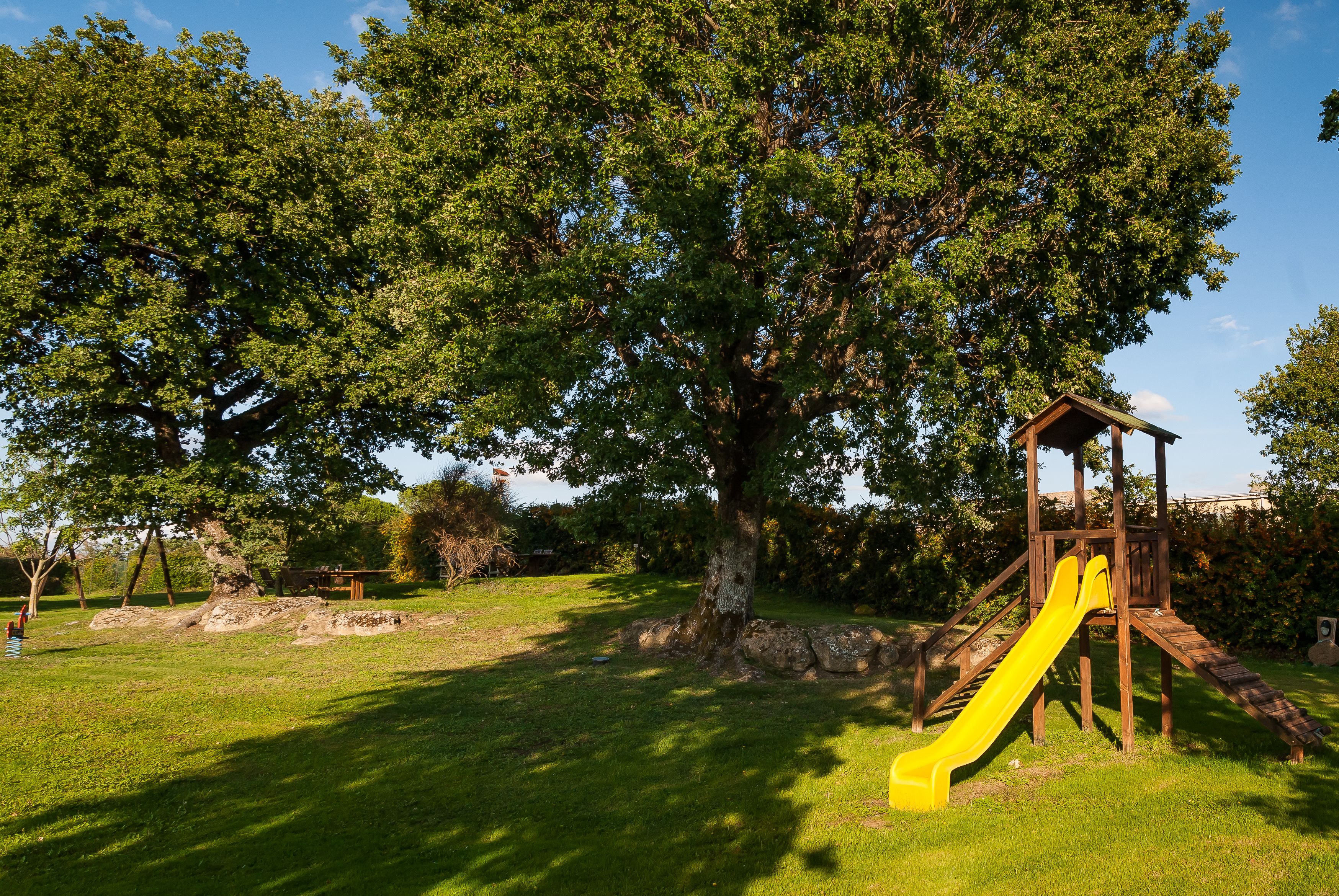 Une aire de jeux avec un toboggan jaune, entourée d’herbe verte et d’arbres.