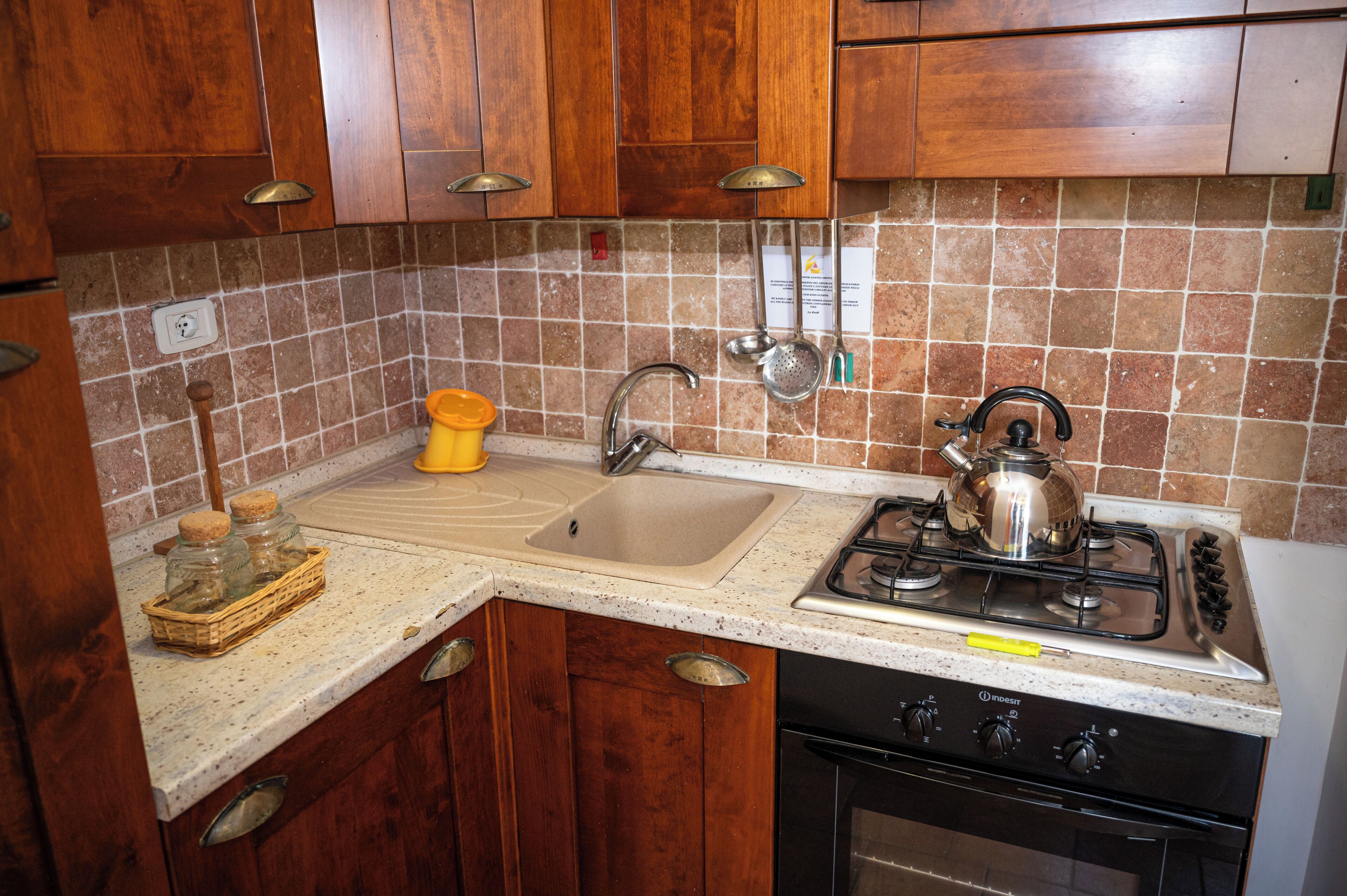 A kitchen with wooden cabinets, a stainless steel sink, a gas stove, and a tiled backsplash.