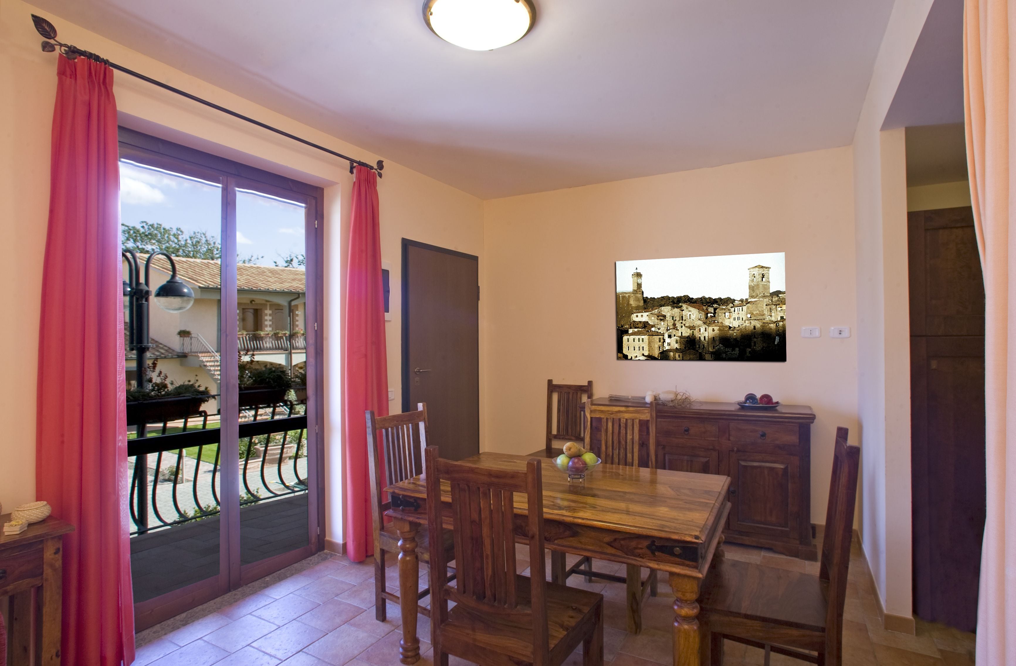 A dining area with a wooden table and chairs, a small fruit bowl, and a view of a town through a window.